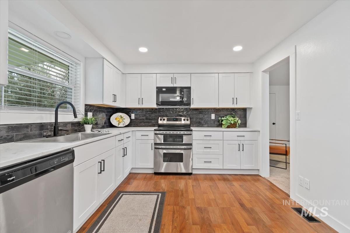 Kitchen featuring white cabinets, stainless steel appliances, tasteful backsplash, light wood-style floors, and light stone counters