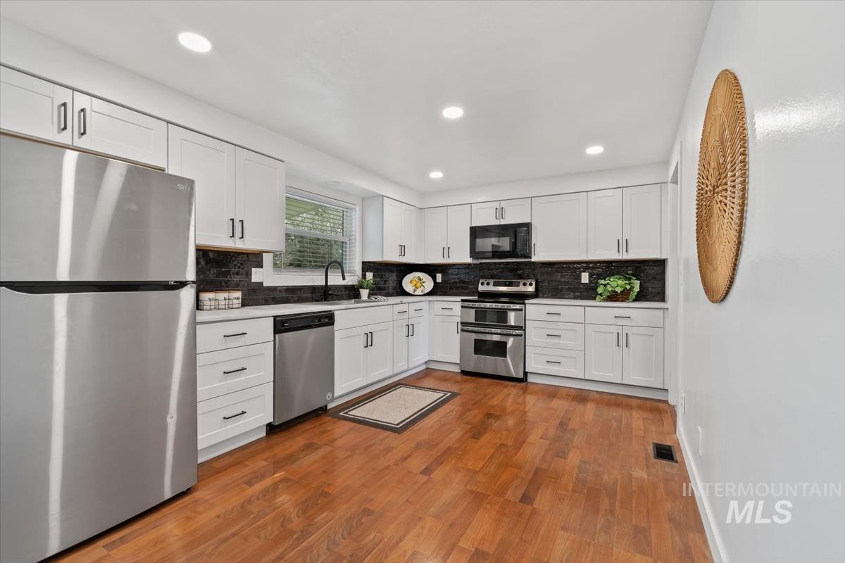 Kitchen with stainless steel appliances, white cabinetry, backsplash, dark wood-type flooring, and recessed lighting