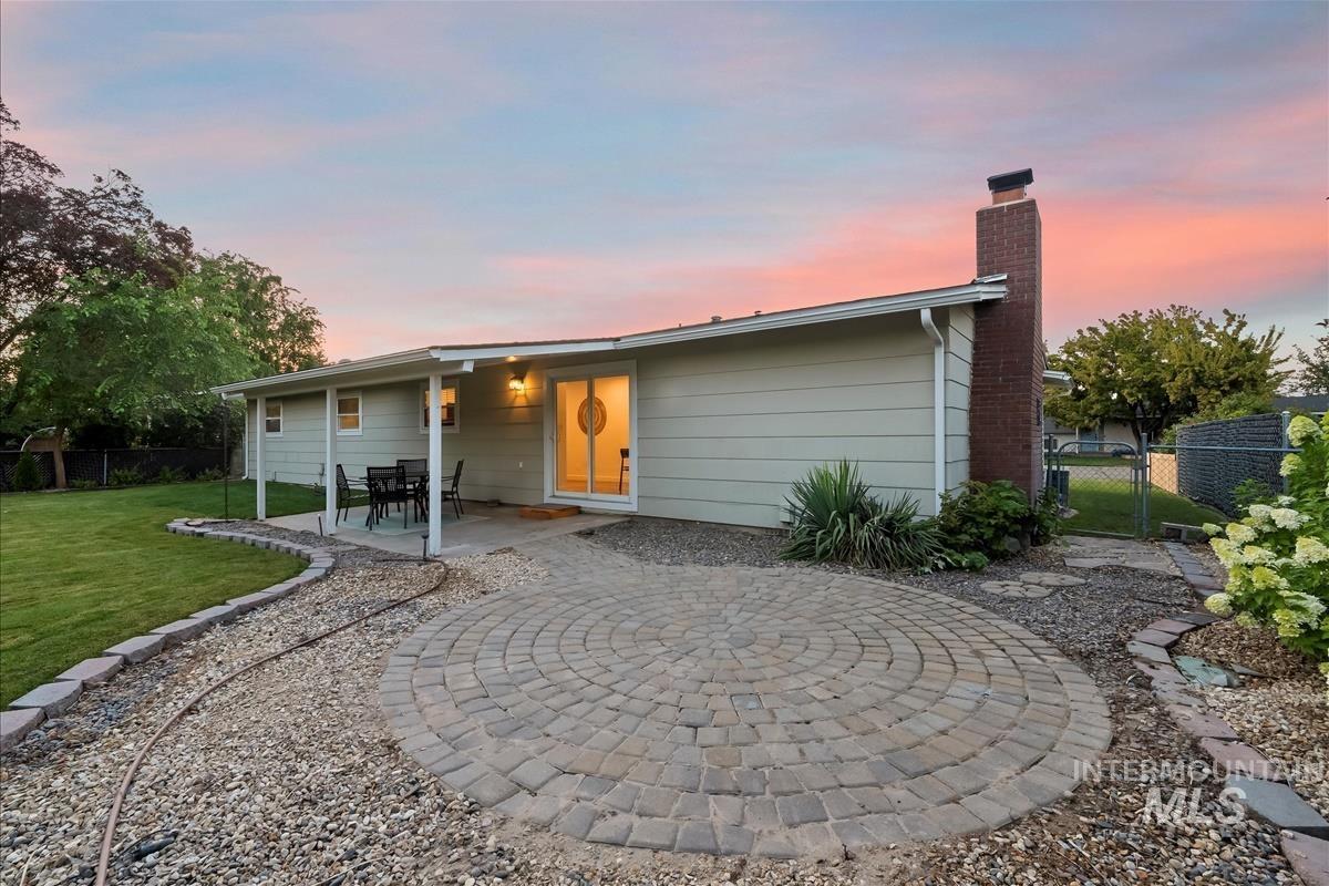 Back of property at dusk featuring a patio, a chimney, and a gate