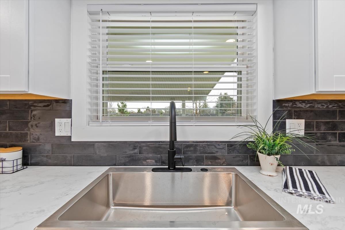 Kitchen view of decorative backsplash, white cabinetry, and light stone counters