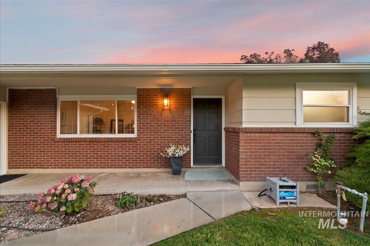 Entrance to property featuring a porch, brick siding, and lawncare items