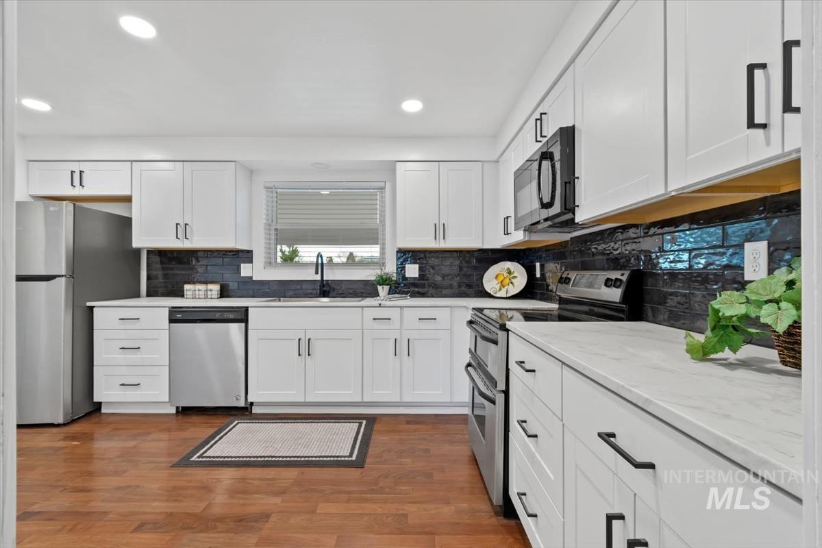 Kitchen featuring appliances with stainless steel finishes, white cabinets, dark wood finished floors, decorative backsplash, and recessed lighting