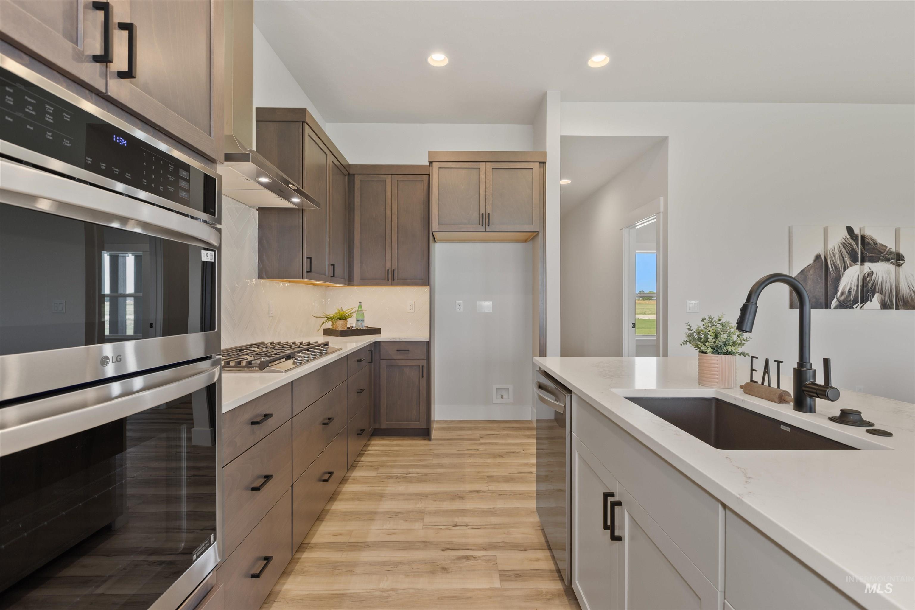Kitchen featuring stainless steel appliances, recessed lighting, light wood-style floors, light stone countertops, and tasteful backsplash