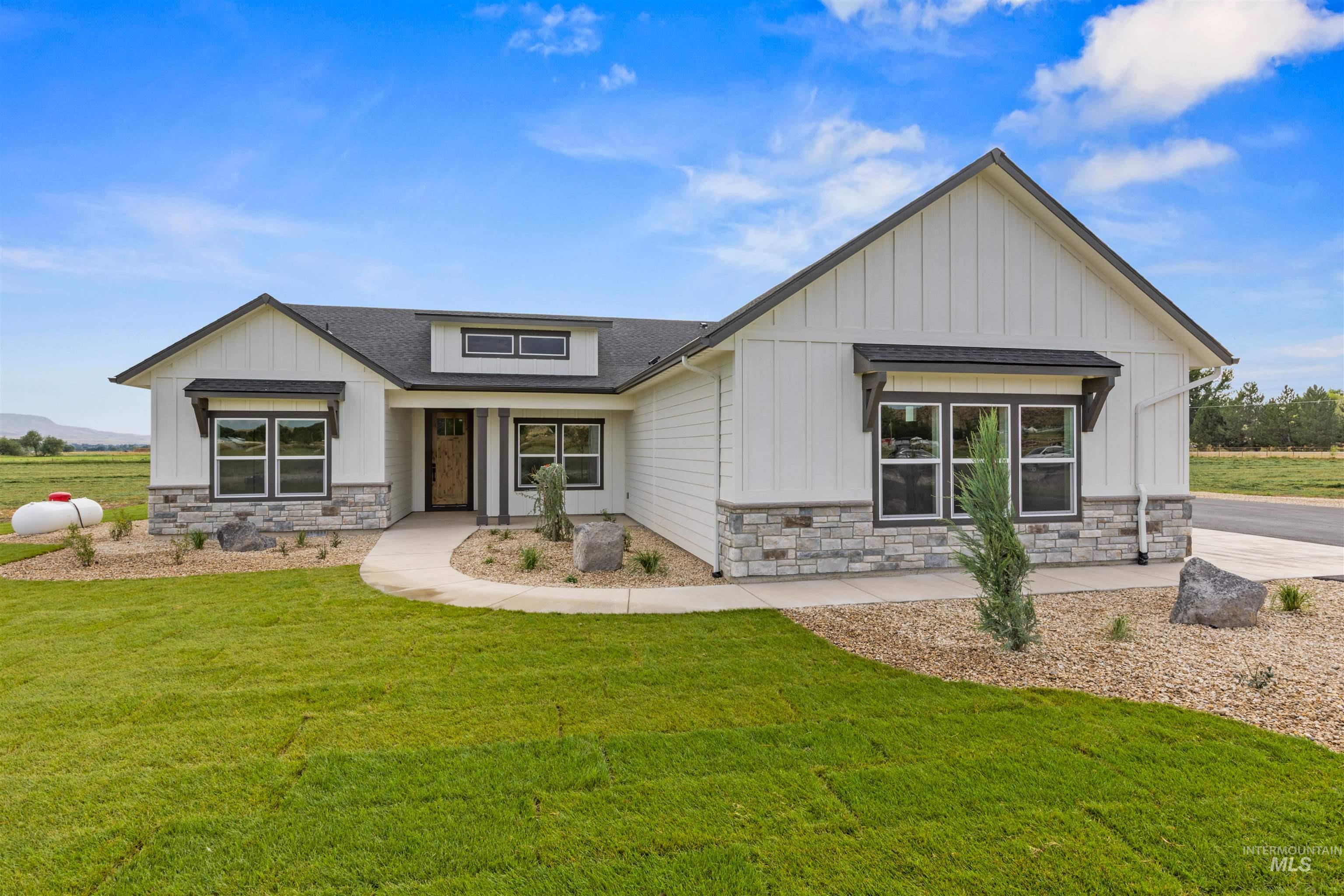 Modern farmhouse style home featuring stone siding, board and batten siding, a front yard, and roof with shingles