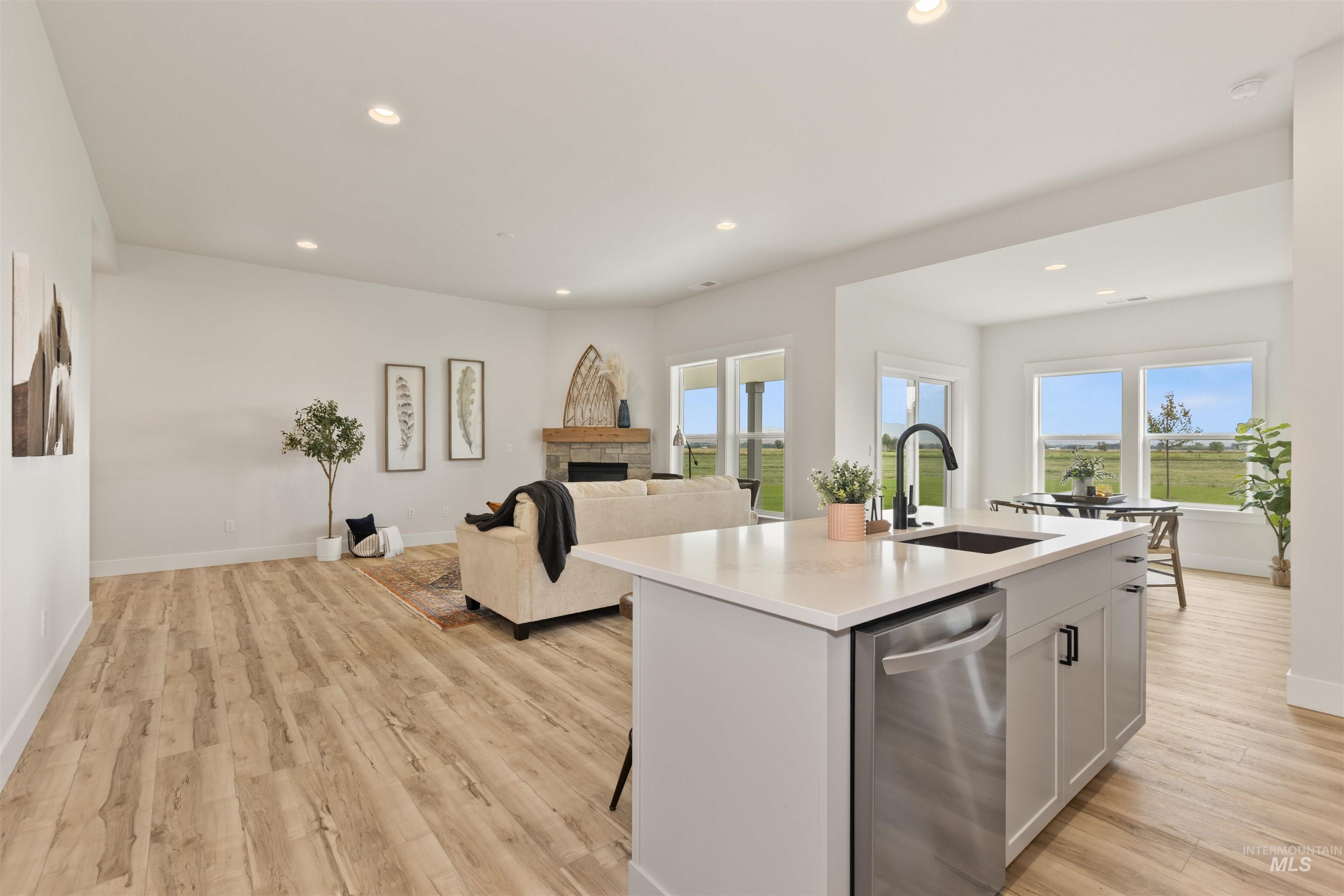 Kitchen featuring recessed lighting, stainless steel dishwasher, open floor plan, an island with sink, and a stone fireplace