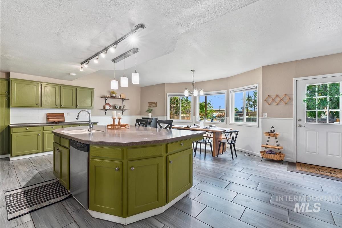 Kitchen with green cabinetry, wood tiled floors, a textured ceiling, a center island with sink, and dishwasher
