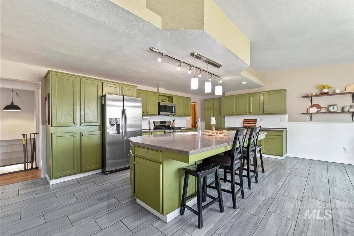 Kitchen with green cabinetry, appliances with stainless steel finishes, hanging light fixtures, track lighting, and a breakfast bar area