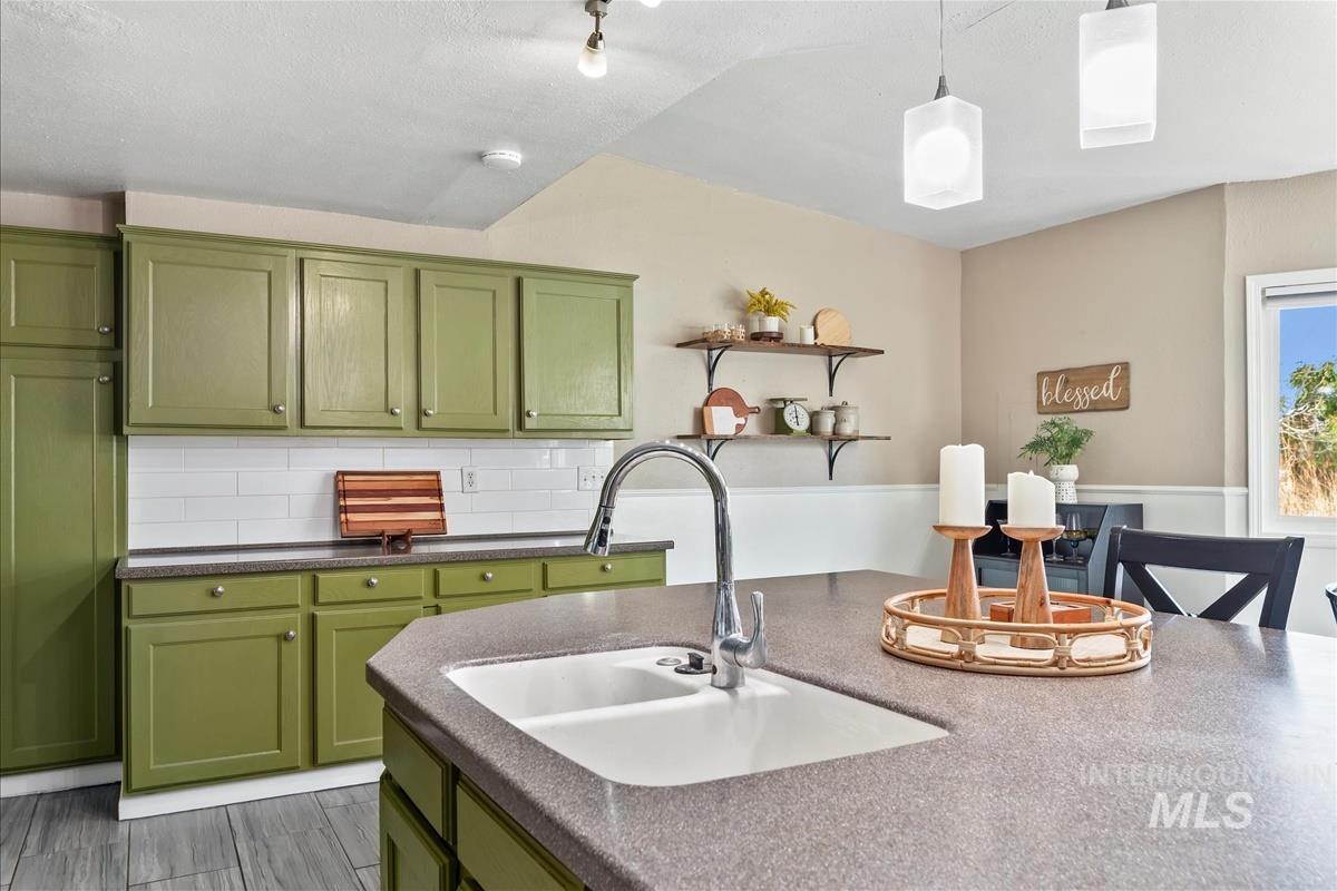 Kitchen featuring green cabinets, backsplash, pendant lighting, and open shelves
