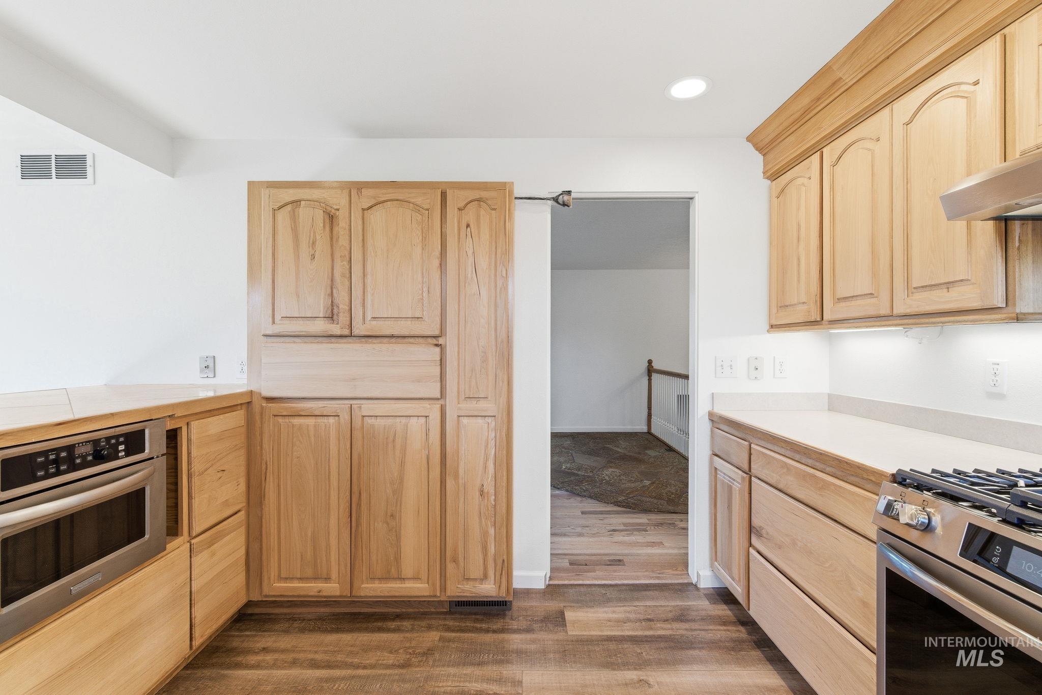 Kitchen with light wood finish cabinetry, light countertops, stainless steel appliances, dark wood-type flooring, and recessed lighting
