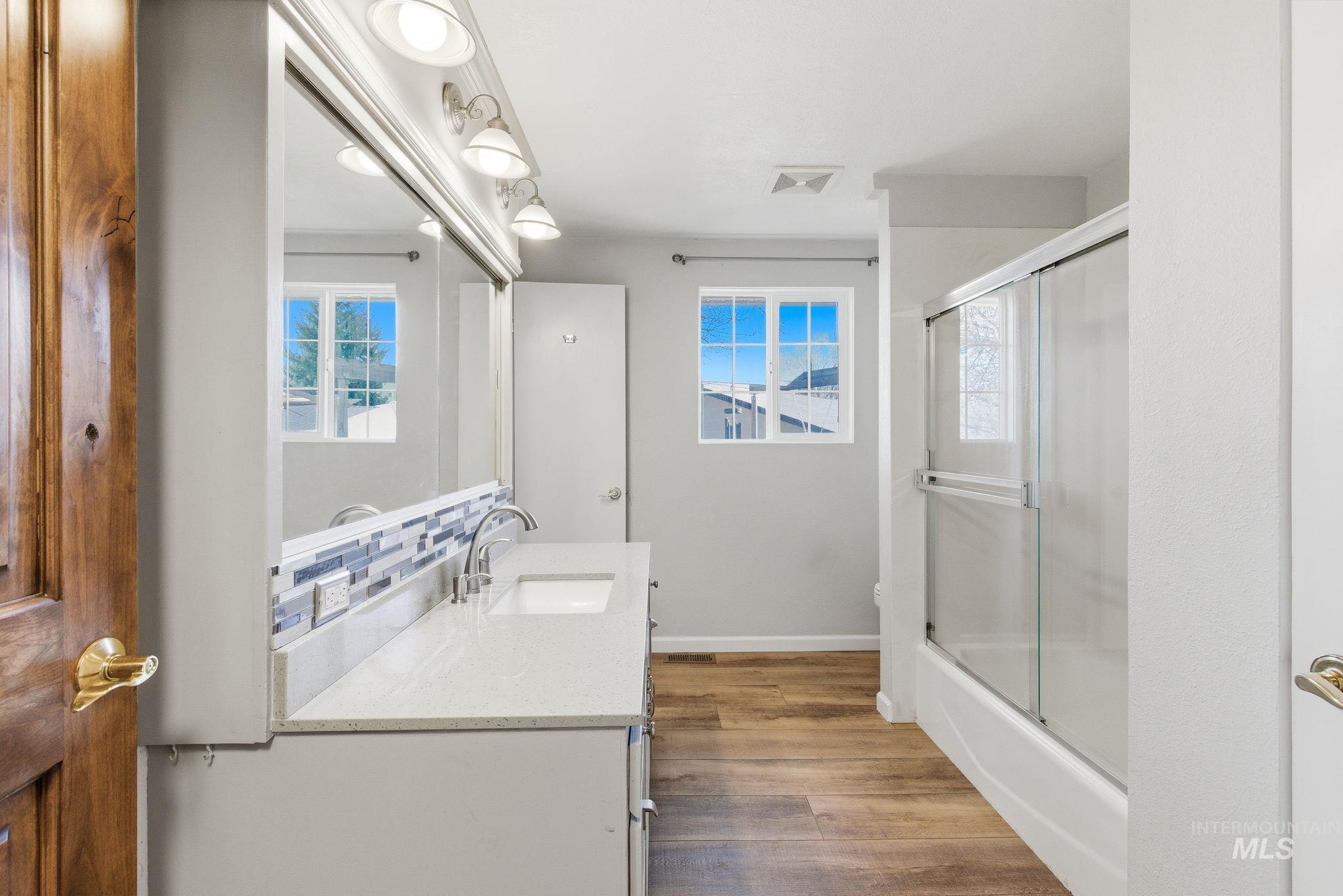 Bathroom featuring vanity, dark wood-style floors, combined bath / shower with glass door, and plenty of natural light