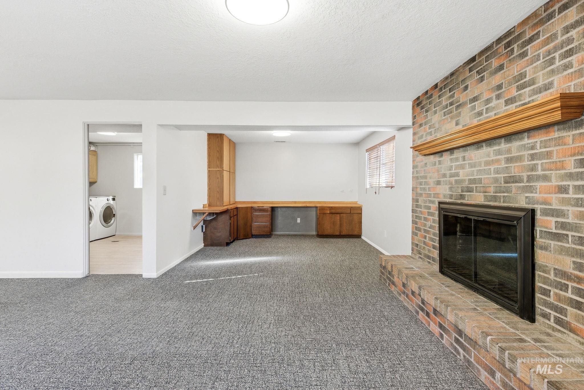 Unfurnished living room with a brick fireplace, dark carpet, built in desk, washer and clothes dryer, and a textured ceiling