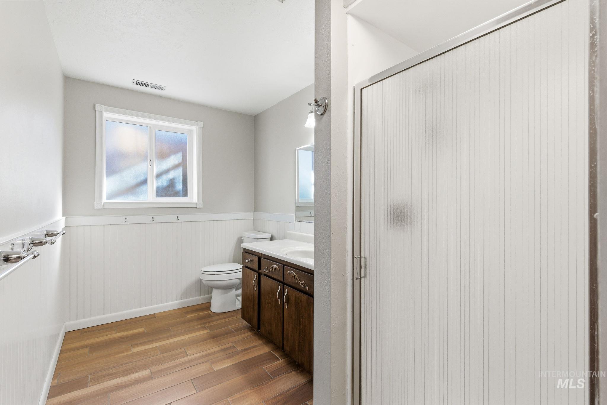 Full bath featuring a wainscoted wall, a shower stall, light wood finished floors, and vanity