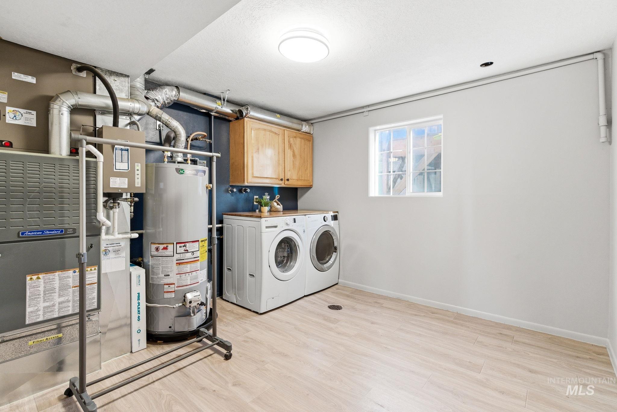 Laundry area featuring light wood finished floors, cabinet space, gas water heater, washing machine and clothes dryer, and heating unit