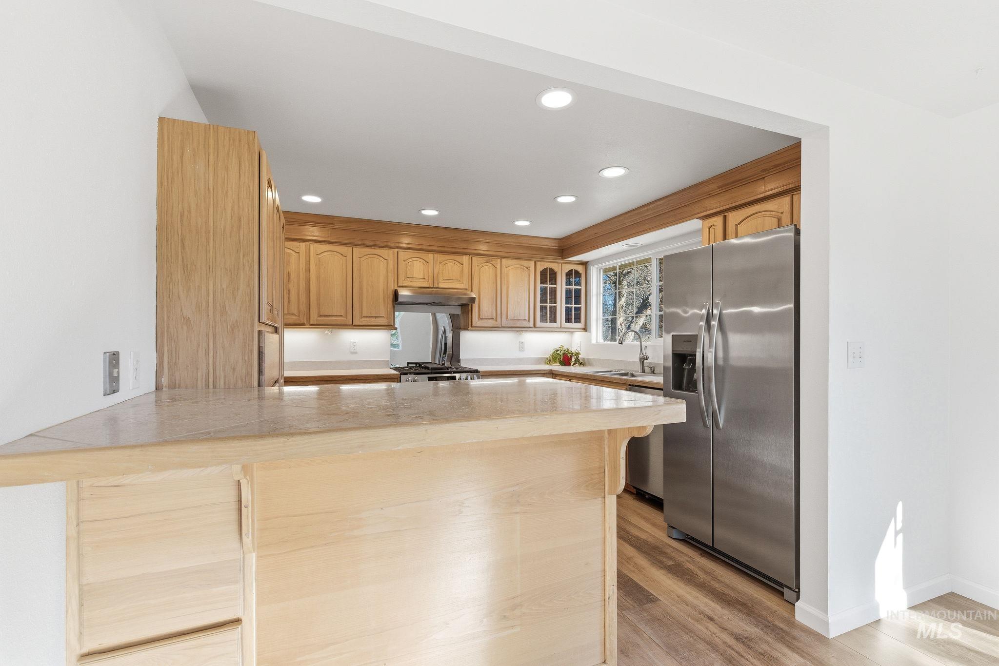 Kitchen with stainless steel appliances, light countertops, recessed lighting, a peninsula, and light wood finished floors