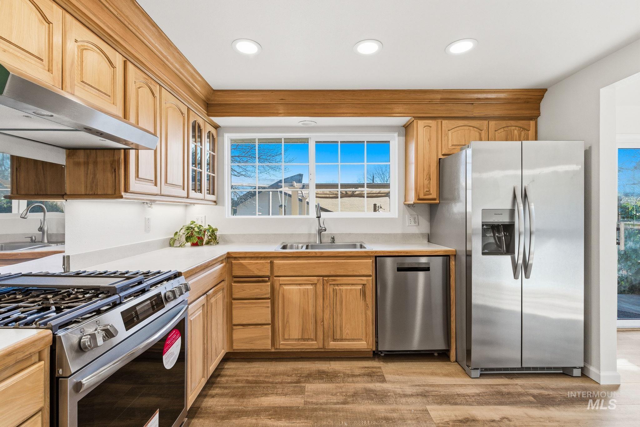 Kitchen featuring stainless steel appliances, light countertops, glass insert cabinets, light wood finished floors, and recessed lighting