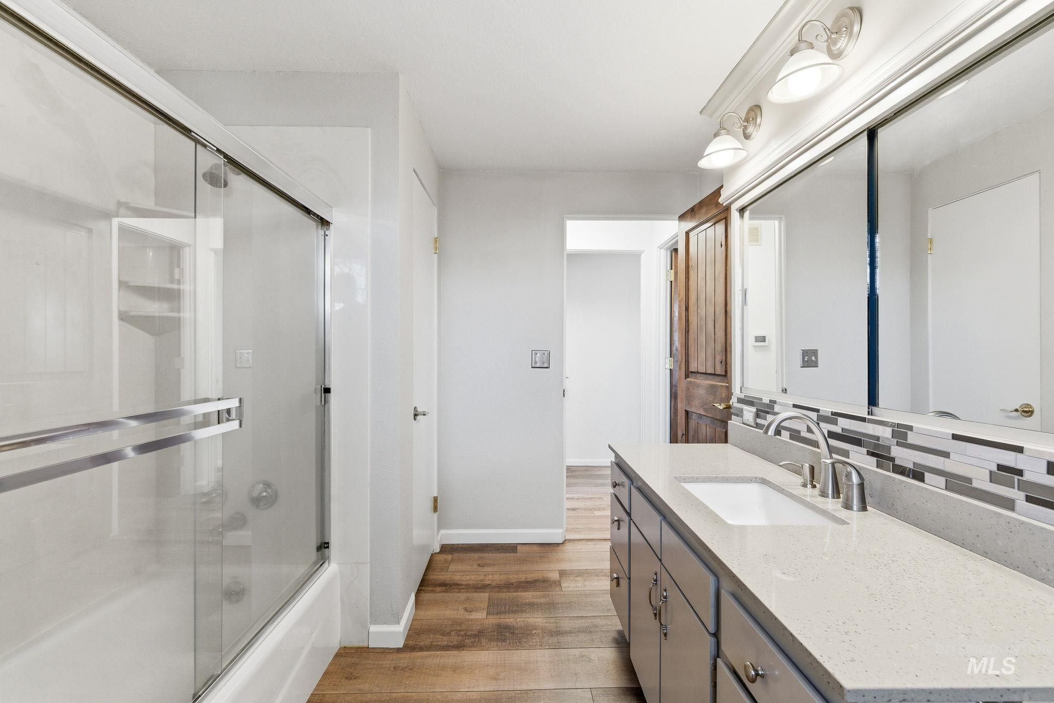 Bathroom with vanity, combined bath / shower with glass door, and light wood-style floors