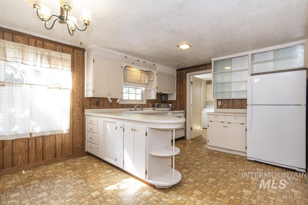 Kitchen featuring open shelves, wood walls, white appliances, light countertops, and a peninsula