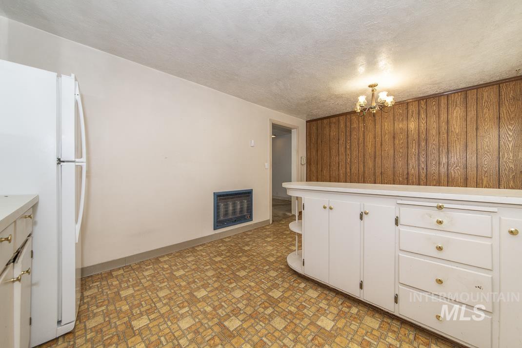 Kitchen with freestanding refrigerator, wood walls, heating unit, light countertops, and a textured ceiling