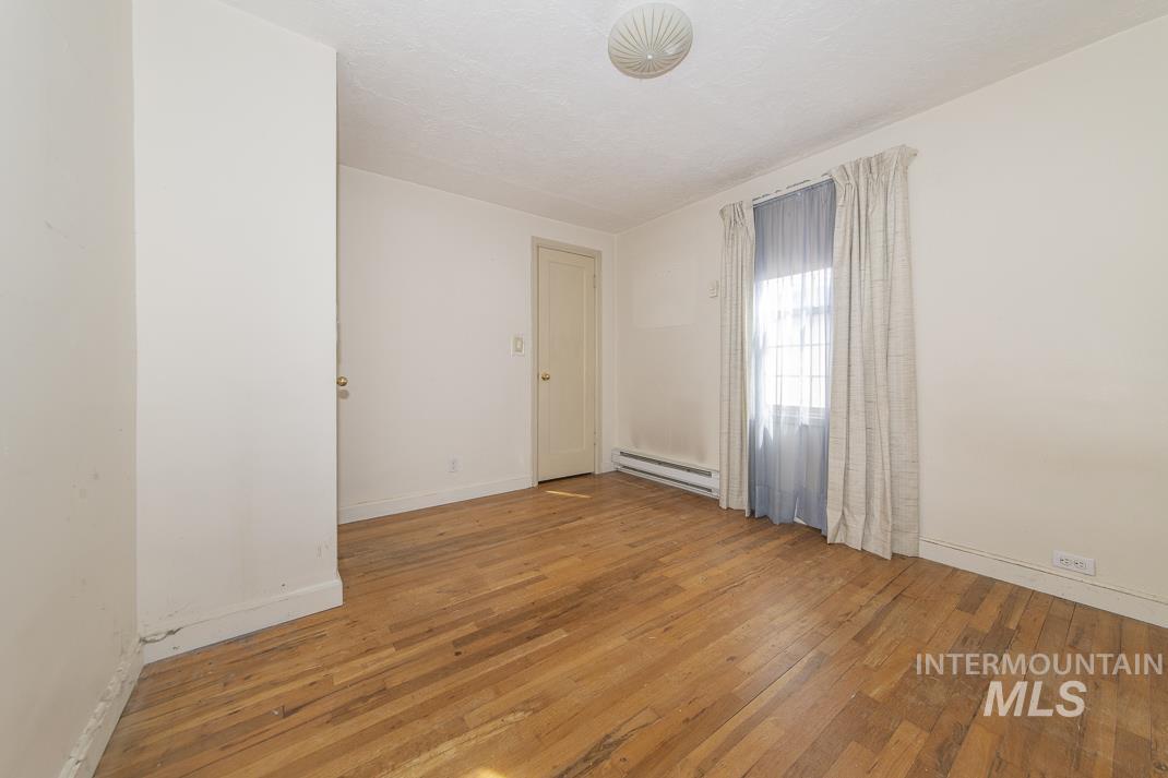 Spare room with light wood-style floors, a baseboard radiator, and a textured ceiling
