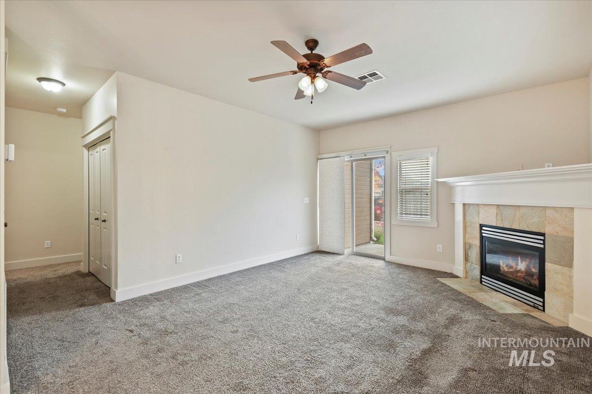 Unfurnished living room featuring carpet, a tiled fireplace, and ceiling fan