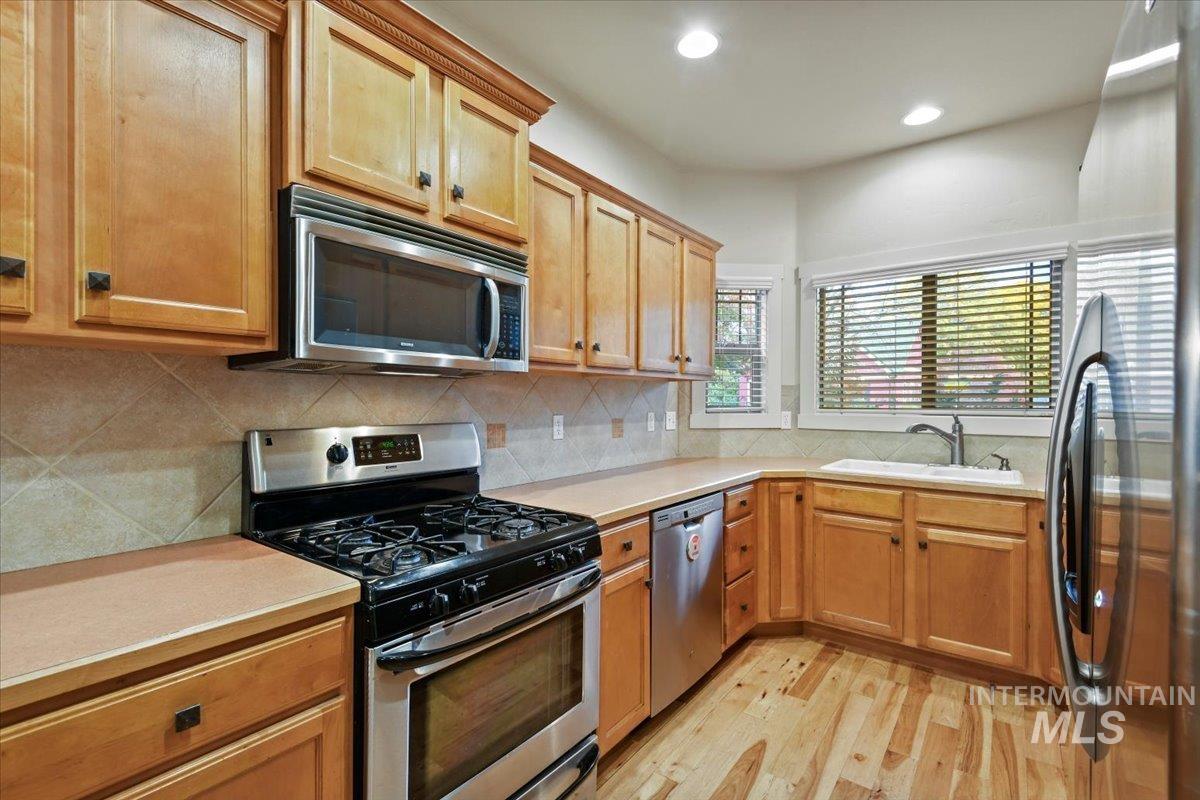 Kitchen with appliances with stainless steel finishes, light countertops, backsplash, light wood-type flooring, and recessed lighting