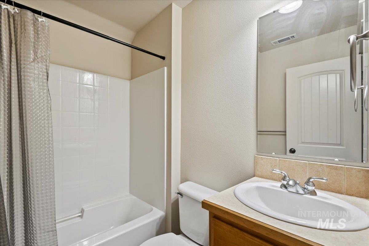 Full bathroom featuring shower / bath combination with curtain, vanity, a textured wall, and decorative backsplash