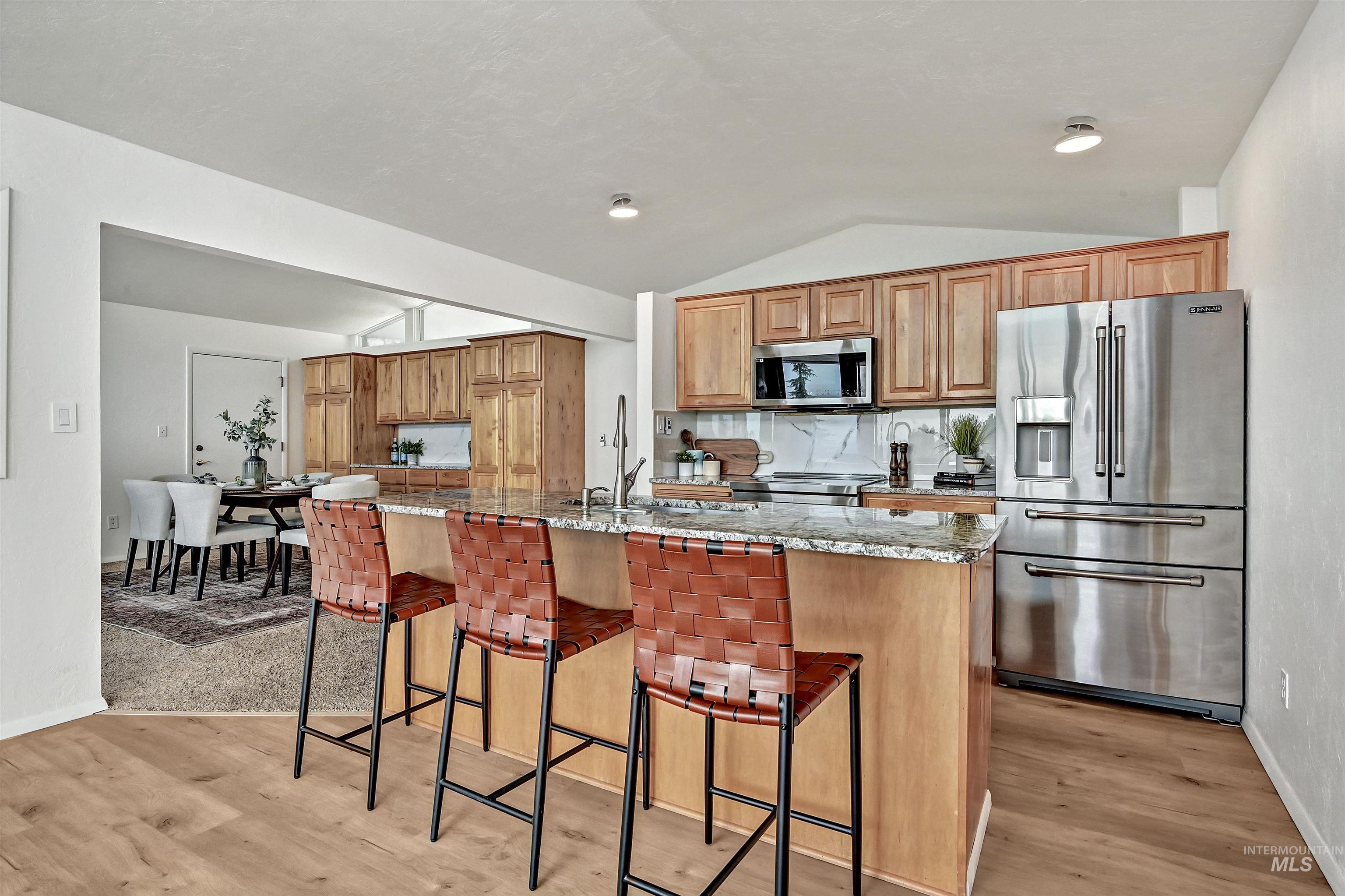 Kitchen with light stone countertops, stainless steel appliances, vaulted ceiling, a kitchen bar, and decorative backsplash