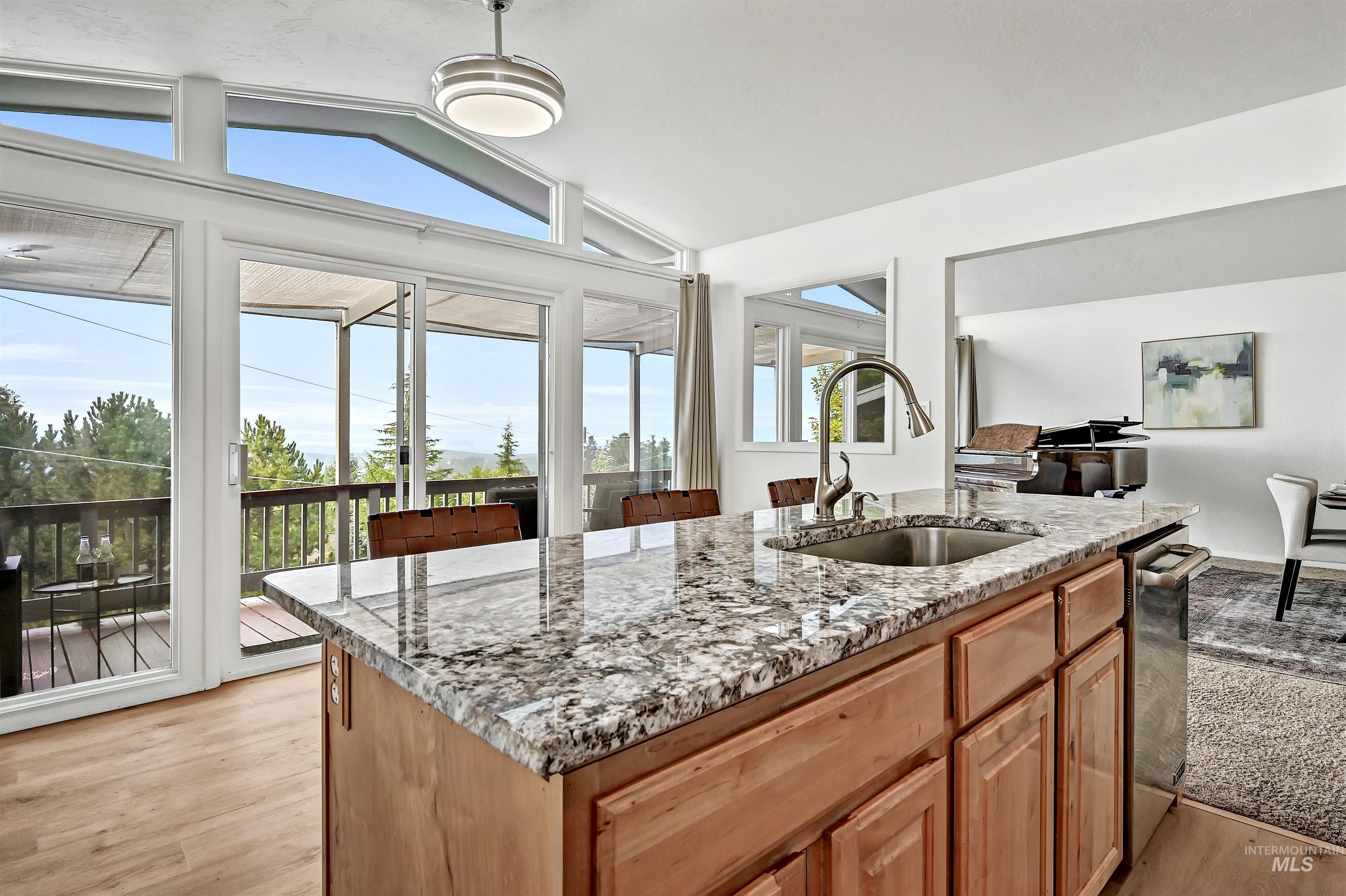 Kitchen with an island with sink, light stone counters, lofted ceiling, light wood-type flooring, and stainless steel dishwasher