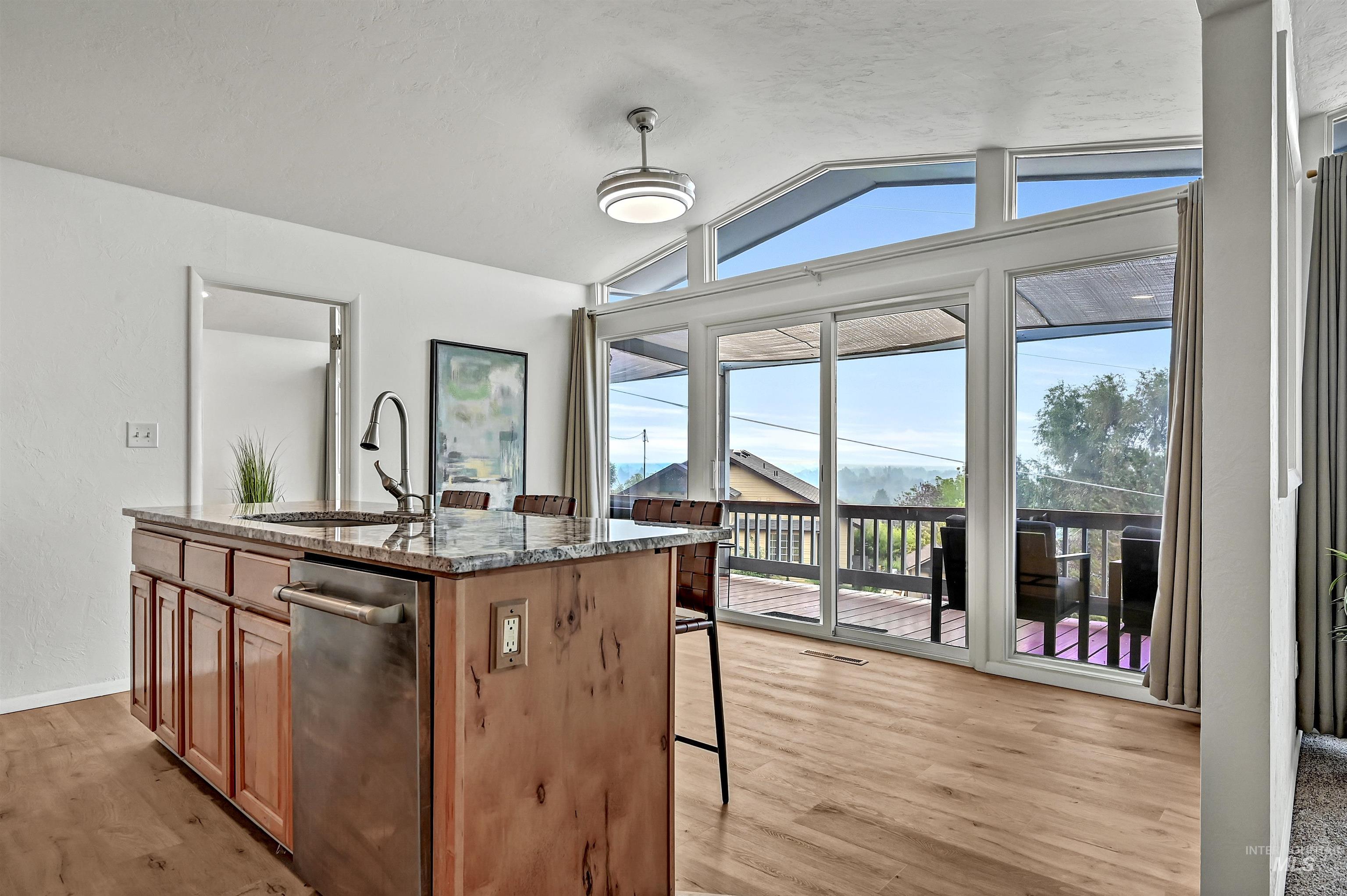 Kitchen with dark stone counters, a kitchen island with sink, lofted ceiling, light wood finished floors, and a kitchen breakfast bar