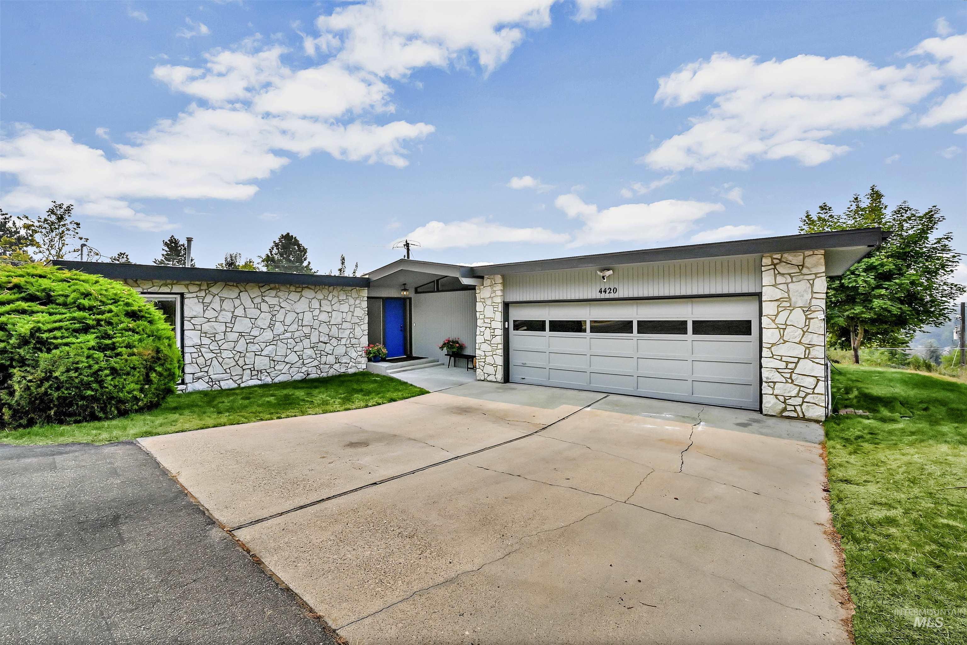 Mid-century inspired home featuring stone siding, driveway, a garage, and a front yard