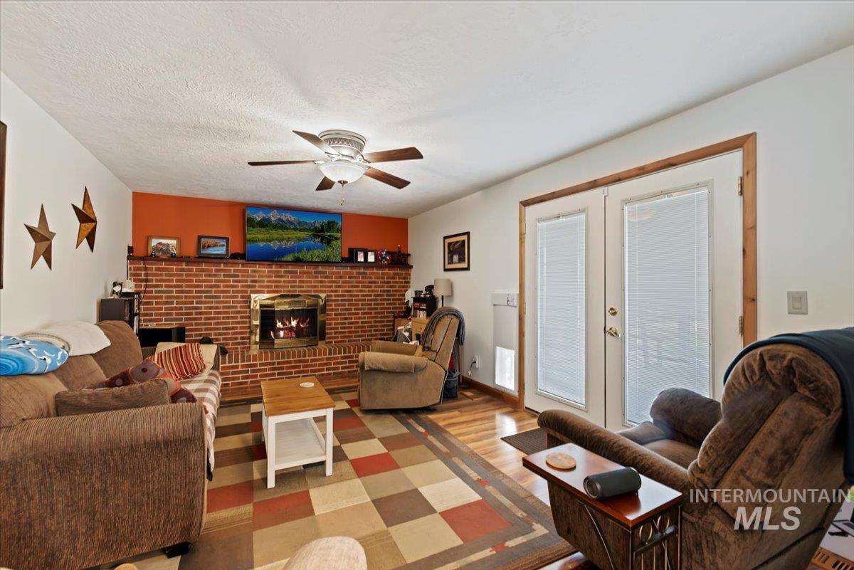 Living area with wood finished floors, a brick fireplace, a ceiling fan, french doors, and a textured ceiling