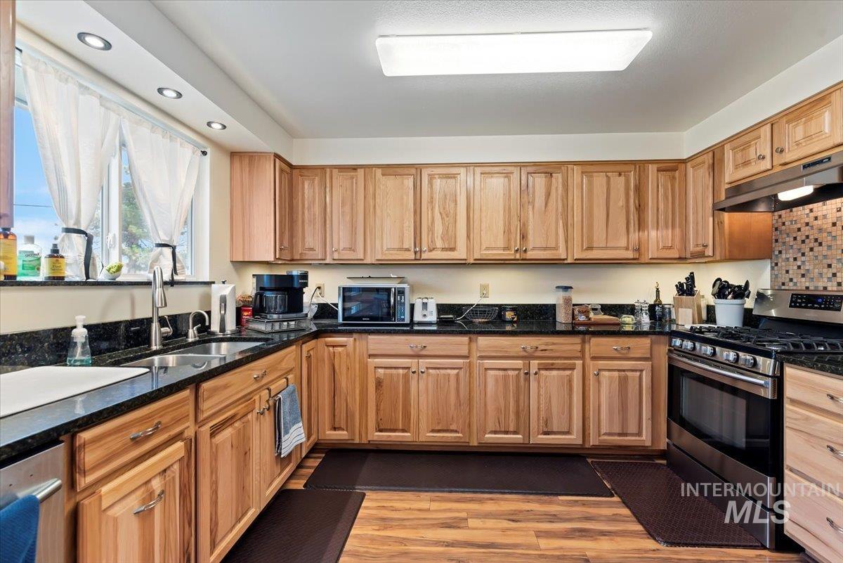 Kitchen with stainless steel appliances, dark stone countertops, under cabinet range hood, light wood-style floors, and recessed lighting