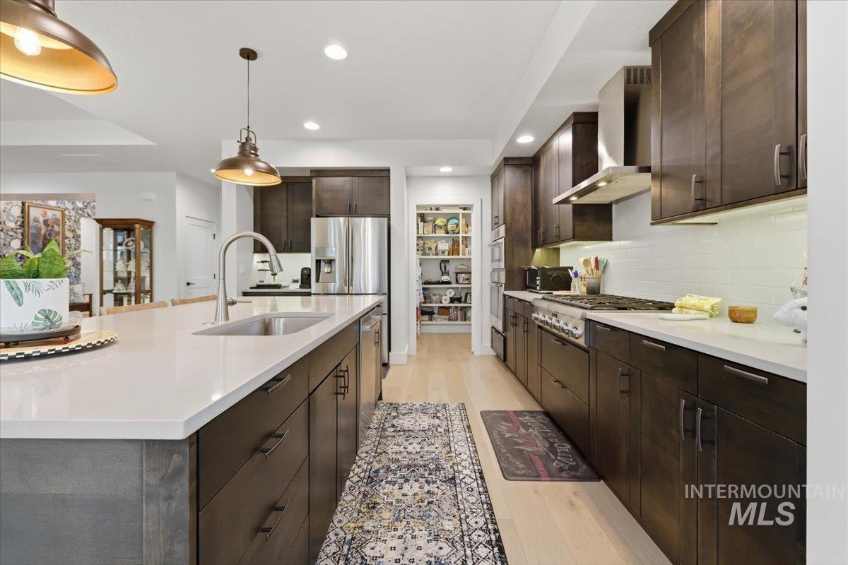 Kitchen with dark wood finish cabinetry, light wood-style flooring, a center island with sink, stainless steel appliances, and light stone countertops