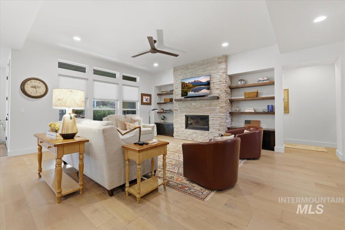 Living room with light wood finished floors, a fireplace, a ceiling fan, and built in shelves
