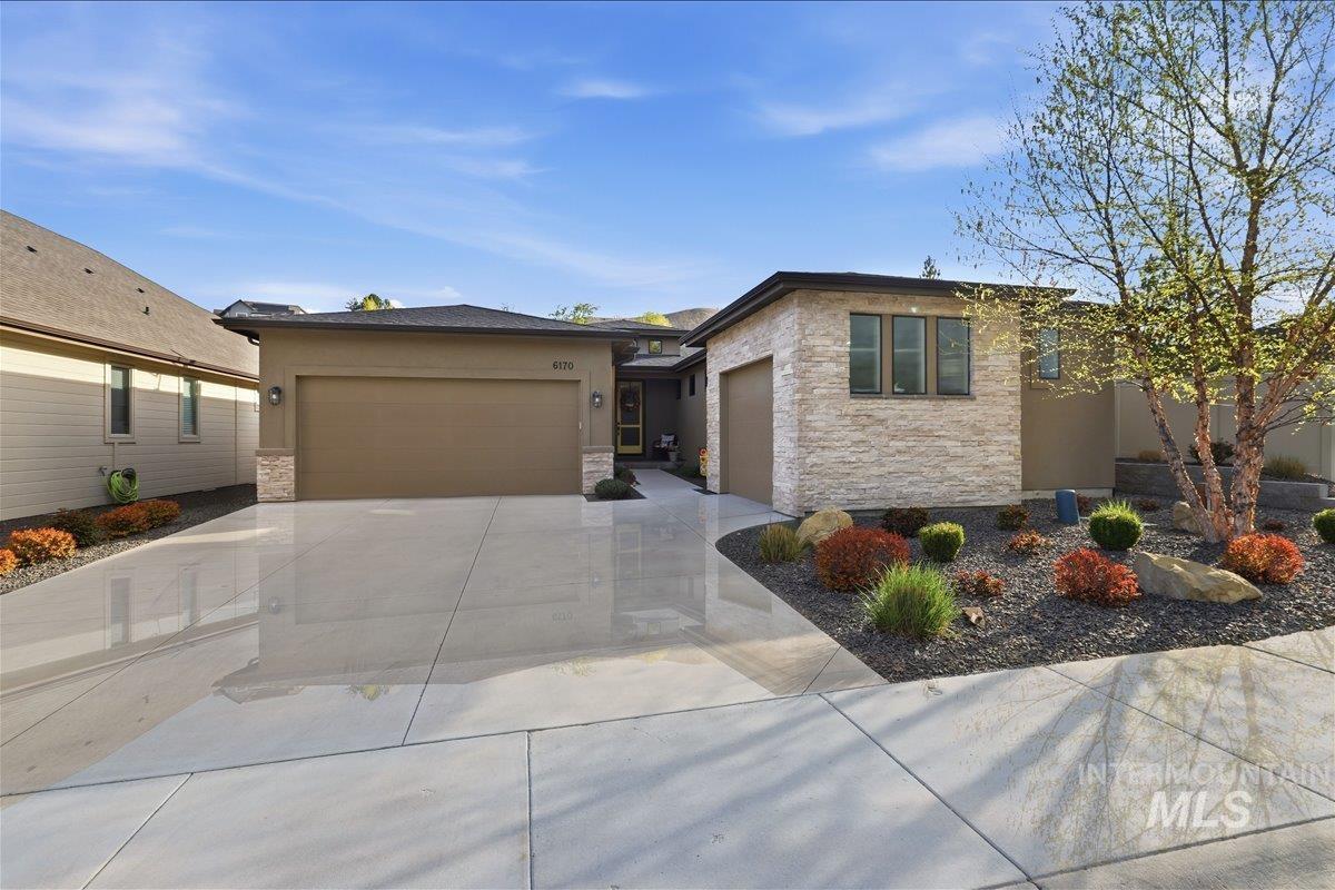 View of front of house with stone siding, driveway, a garage, and stucco siding