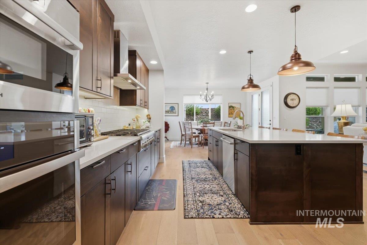 Kitchen featuring dark wood finish cabinets, light wood-type flooring, stainless steel appliances, and backsplash