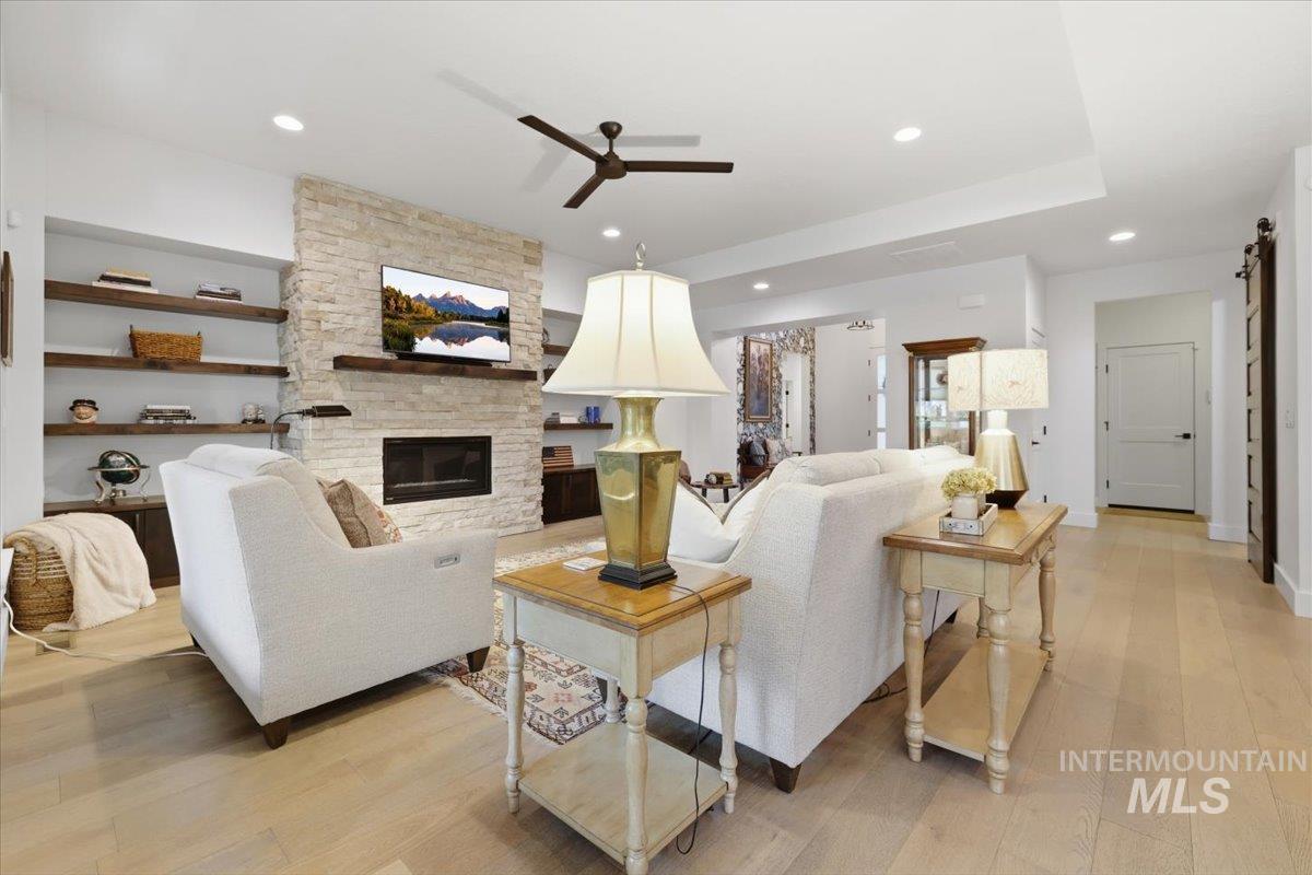 Living area featuring light wood-style flooring, a barn door, a fireplace, ceiling fan, and recessed lighting