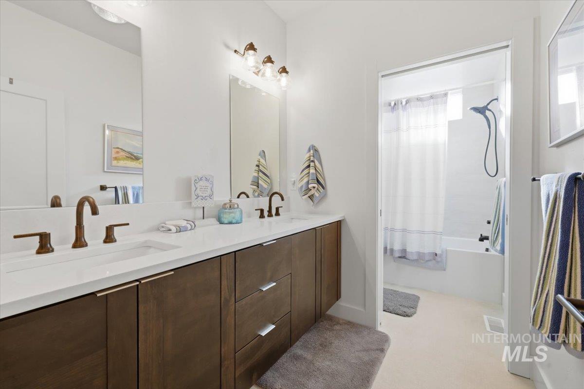 Bathroom featuring double vanity, shower / bath combination with curtain, and light carpet