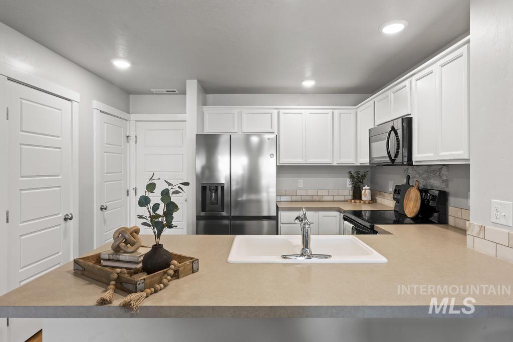 Kitchen featuring black appliances, light countertops, white cabinetry, a peninsula, and recessed lighting