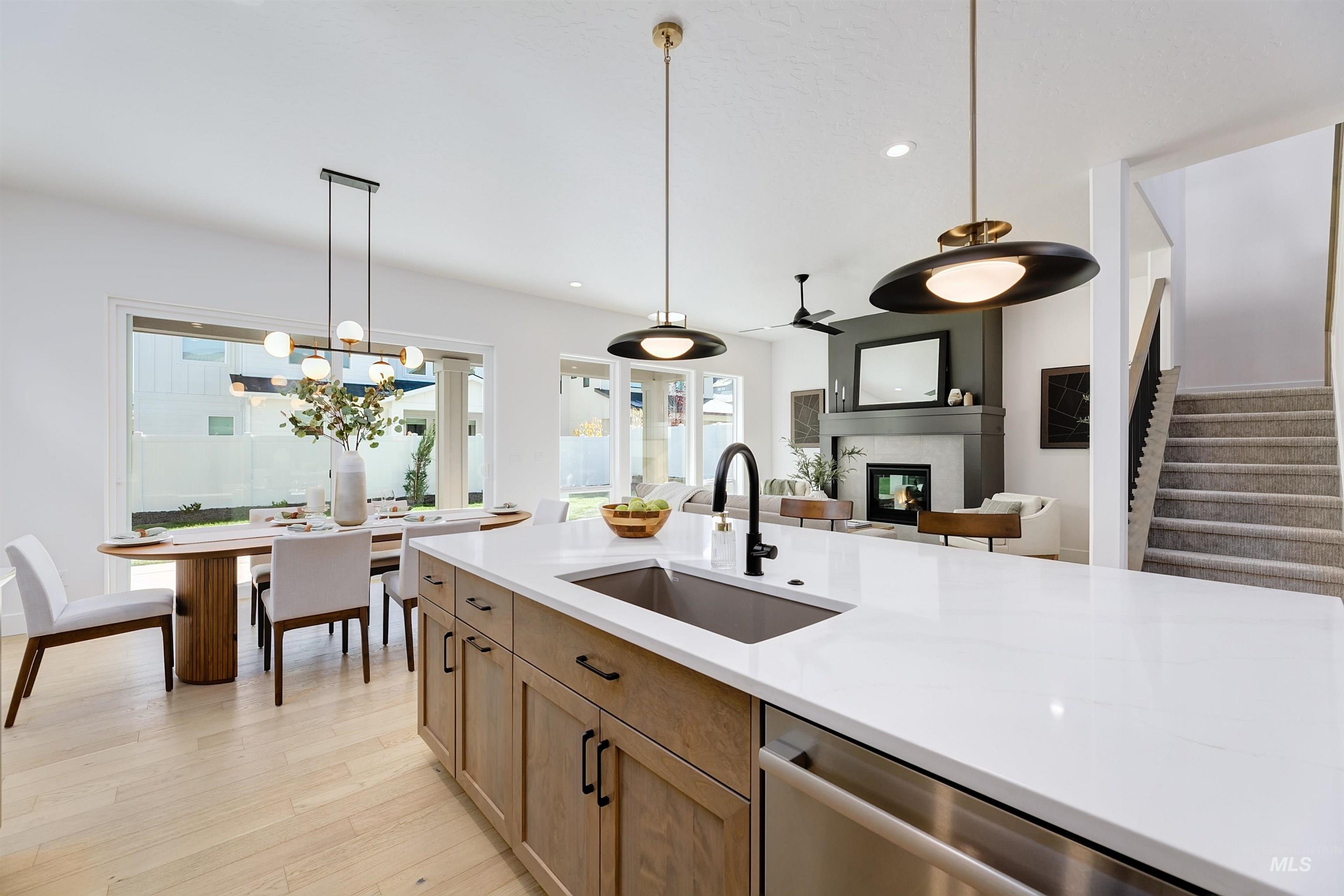 Kitchen with decorative light fixtures, stainless steel dishwasher, light wood finished floors, recessed lighting, and a glass covered fireplace