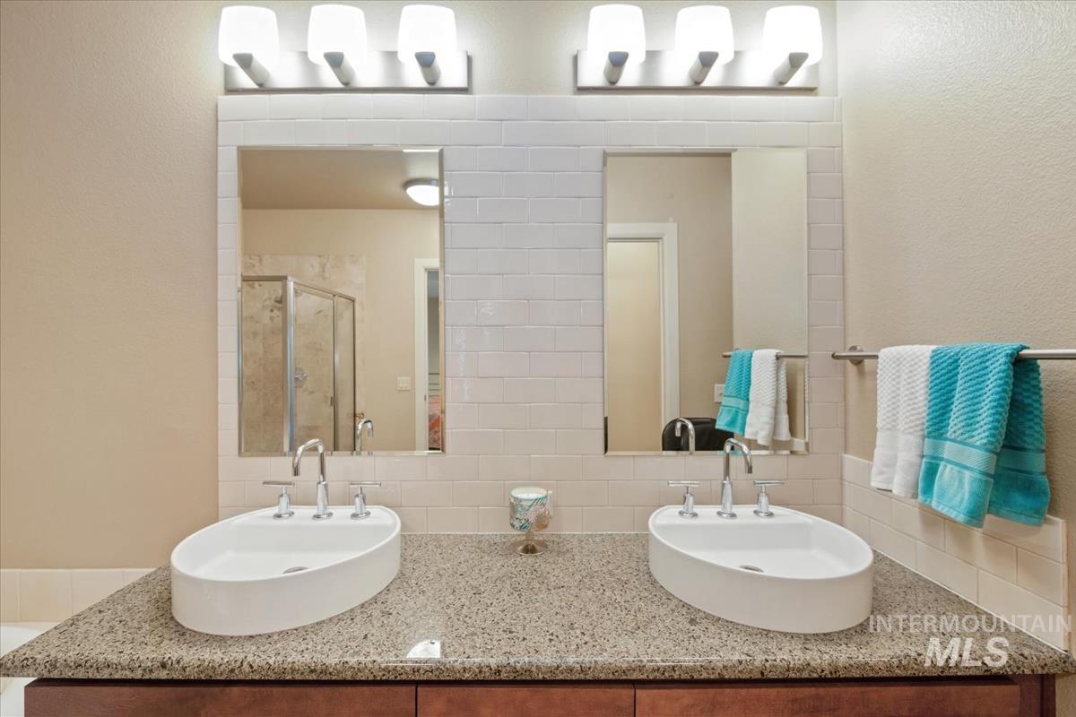 Bathroom featuring a stall shower, double vanity, tasteful backsplash, and a textured wall