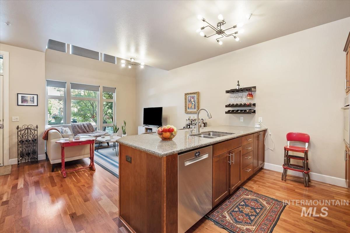 Kitchen featuring brown cabinetry, a peninsula, stainless steel dishwasher, open floor plan, and light wood-style floors
