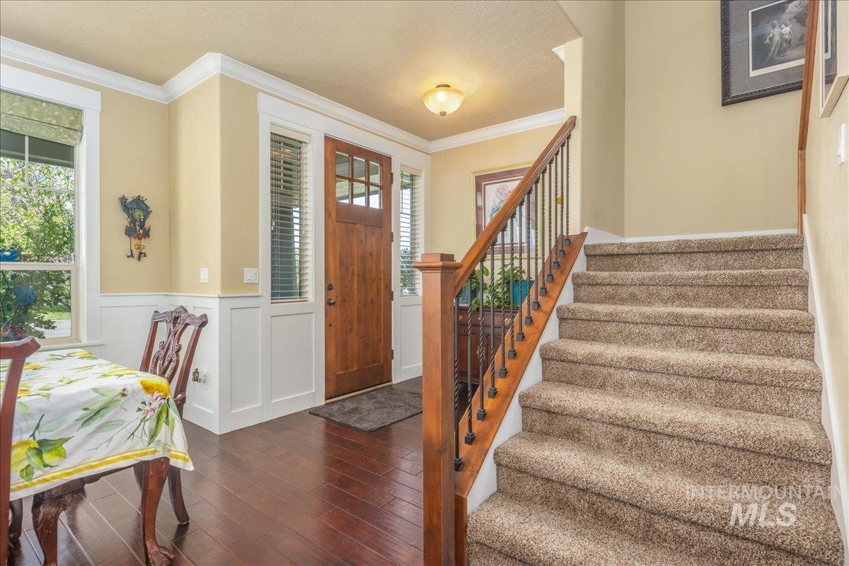 Entryway featuring wood-type flooring, crown molding, a decorative wall, a wainscoted wall, and stairs