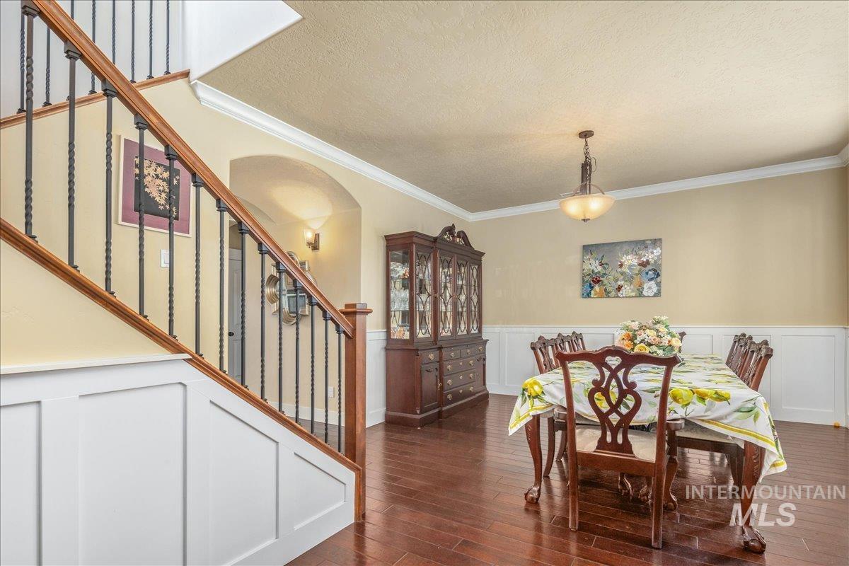 Dining space with wainscoting, a decorative wall, ornamental molding, dark wood finished floors, and stairway