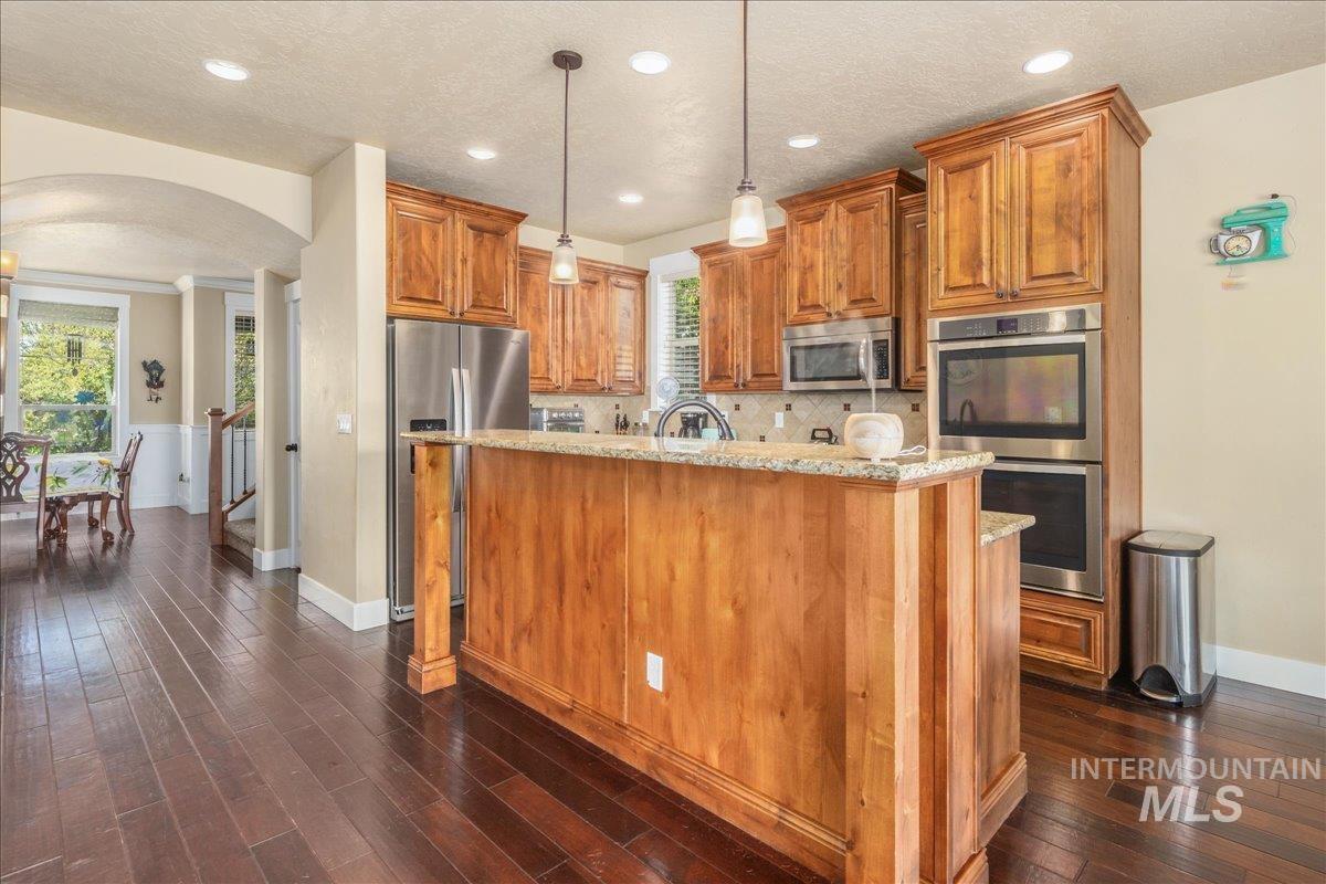 Kitchen featuring arched walkways, appliances with stainless steel finishes, light stone countertops, brown cabinets, and recessed lighting