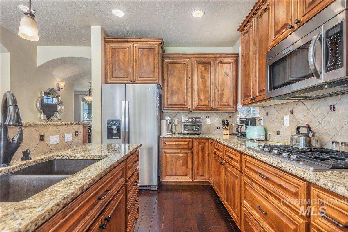 Kitchen with tasteful backsplash, appliances with stainless steel finishes, dark wood finished floors, brown cabinets, and a textured ceiling