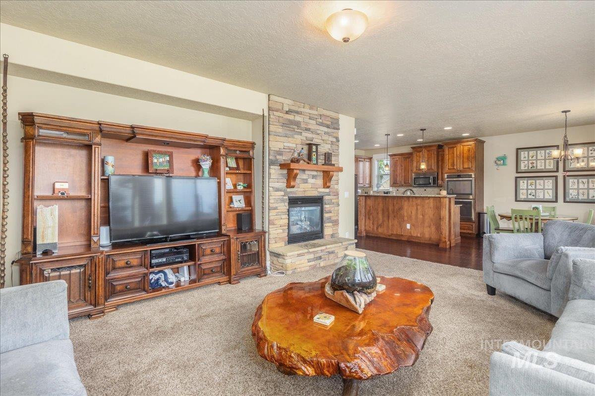 Living area featuring a textured ceiling, a stone fireplace, carpet floors, and a chandelier