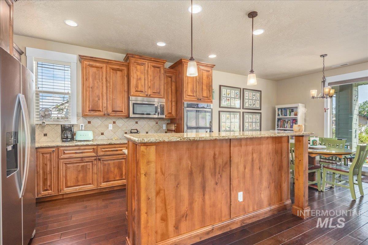 Kitchen with plenty of natural light, stainless steel appliances, a textured ceiling, dark wood-style flooring, and brown cabinets