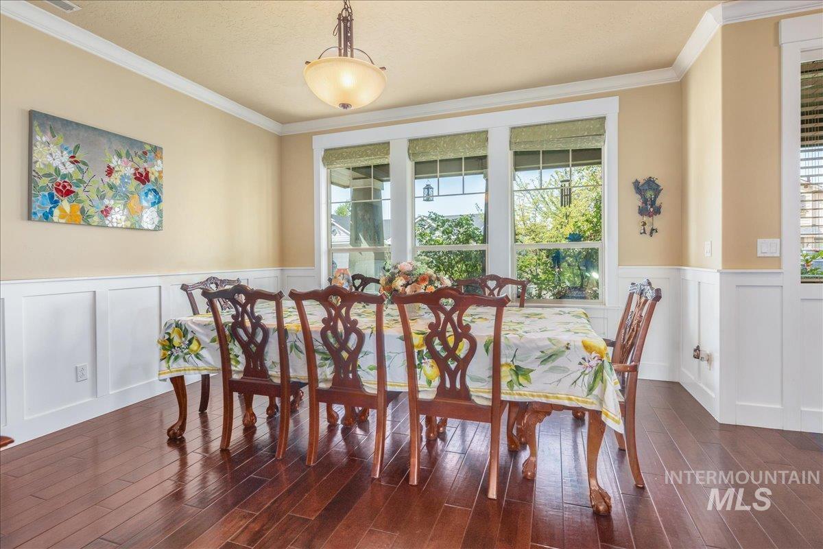 Dining space featuring a decorative wall, a wainscoted wall, ornamental molding, and wood finished floors