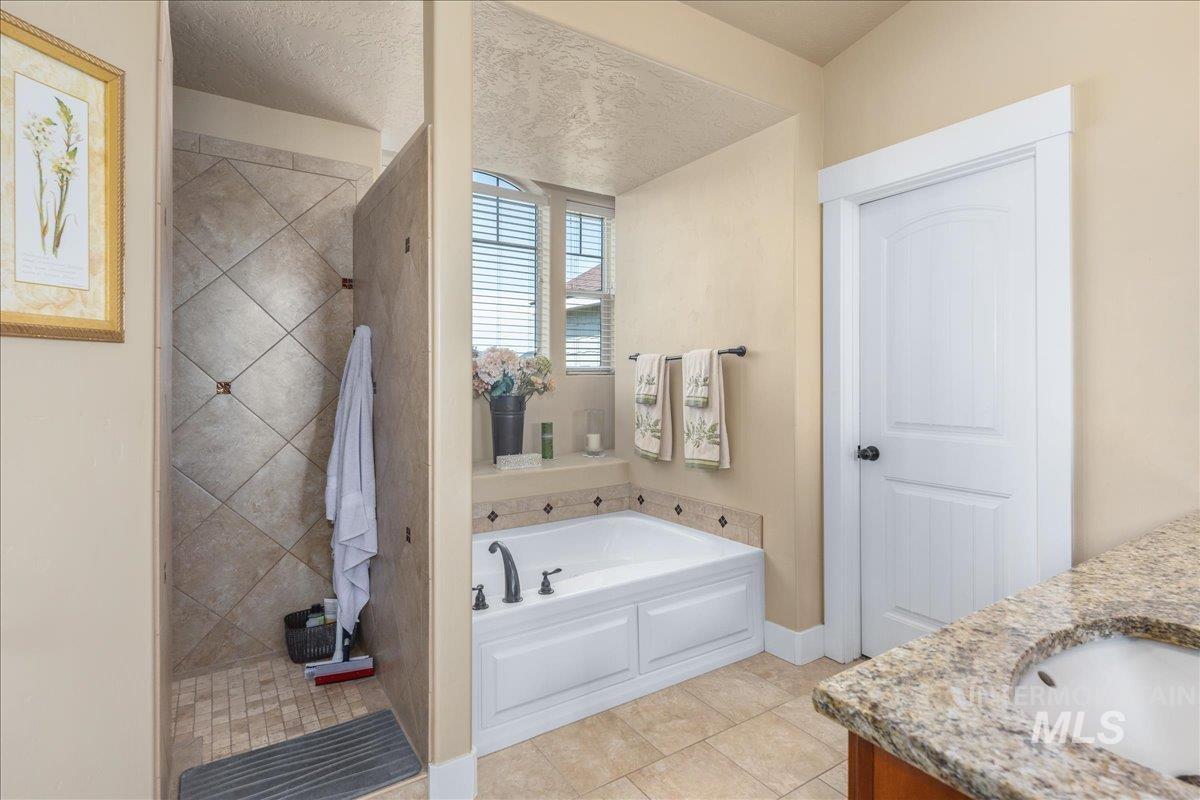 Bathroom featuring vanity, a garden tub, tile patterned flooring, tiled shower, and a textured ceiling